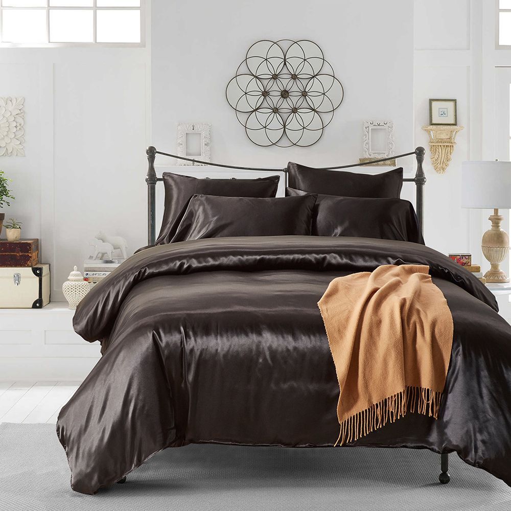 Dark satin bedding with matching pillows and a gold throw in a bright bedroom
