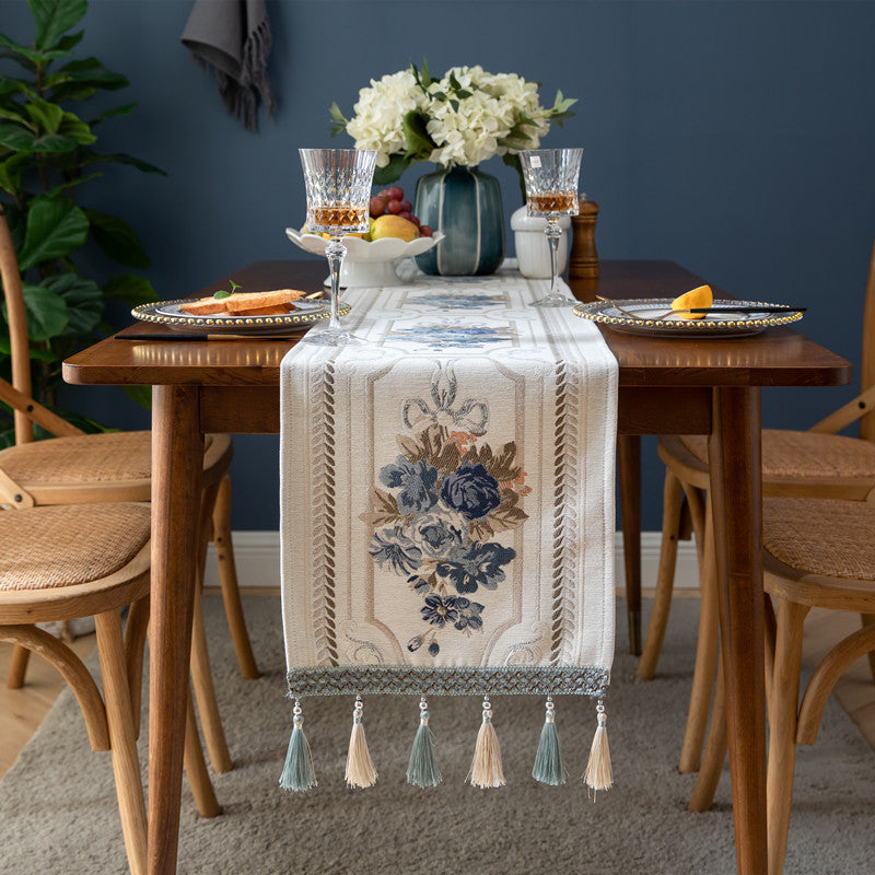 Floral table runner with decorative tassels styled on a wooden dining table.